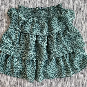 Grön leopardmönstrad volangkjol från Bubbelroom i strl S - Grön leopardmönstrad volangkjol från Bubbelroom i strl S.  Kjolen har en underkjol.  Sparsamt använd och i fint begagnat skick.  Mått Midjan: ca 34 cm Totallängd: ca 50 cm  Polyester  Kommer från ett djur och rökfritt hem.