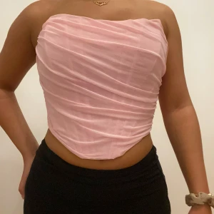 Rosa axelbandslös topp - Säljer en superfin rosa axelbandslös topp. Den är tight och har en snygg draperad design med dragkedja bak. Perfekt för festliga tillfällen 🩷