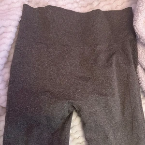 Grå leggings i syntetmaterial - Säljer ett par grå/khakigröna leggings. De är högmidjade och har en tight passform, perfekt för träning eller en avslappnad dag hemma. Materialet är en blandning av polyamid, polyester och elastan vilket gör dem stretchiga och bekväma.