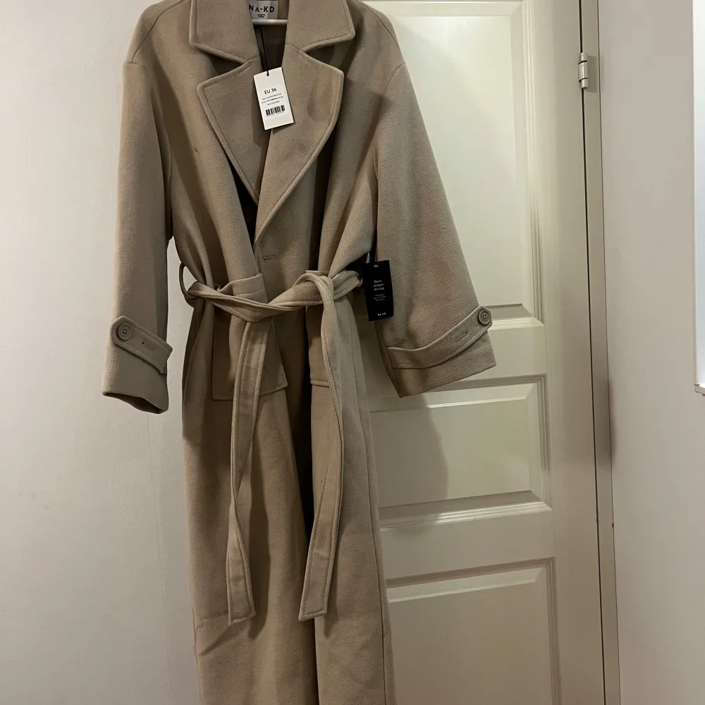 This coat features a wool blend fabric. It has a lapel design and long sleeves with a buckle detail. The coat features front pockets with a patched design, a belt with a self tie detail  and a back slit detail. Originall prize 1099 kr. Sold out. . Jackor.