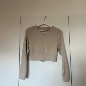 Säljer en superfin beige croppad tröja från Gymshark. Den har långa ärmar och en snygg öppen rygg med snörning som ger en unik look. Perfekt för både träning och vardagsstil. Materialet känns mjukt och stretchigt, vilket gör den bekväma att ha på sig