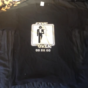 T-shirt  - Kul svart T-shirt med trycket ”game over” och ett par som gifter sig. Köpt på loppis men aldrig använd av mig och är i super bra skick. Fråga om du har frågor!