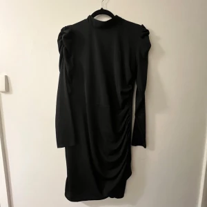 Svart långärmad klänning med rynkdetaljer - Säljer en elegant svart klänning med långa ärmar och en hög hals. Klänningen har snygga rynkdetaljer på sidan som ger en fin form.