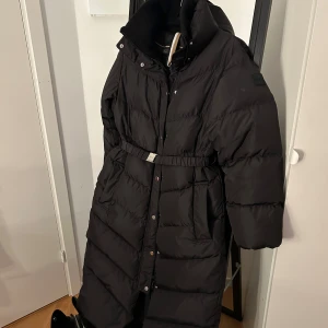 Lång dunkappa  - En lång super fin äkta Hugo Boss dunkappa,perfekt nu till vintern. Den har ingen liva men istället har den en virkad krage på insidan. Den är i storlek 36. Den är använd vintern 2023-2024. Den har inga synliga defekter vad jag kan se. 