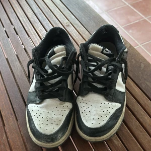 Svartvita sneakers från Nike - Säljer ett par svartvita Nike sneakers med snörning. Skorna har en klassisk design med perforerade detaljer på ovansidan och en robust sula. Perfekta för en avslappnad stil.