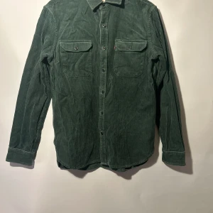 Grön manchester skjorta från Levi's - Snygg grön manchester skjorta från Levi's med klassisk krage och knappar framtill. Skjortan har två bröstfickor med knappstängning och långa ärmar. Perfekt för en stilren look. Storlek s, använd ett fåtal gånger och i  mycket bra skick