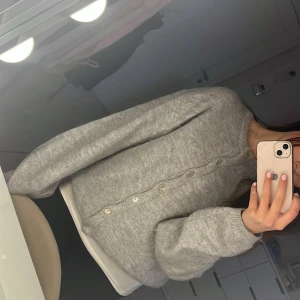 Grå kofta med knappar - Säljer en mysig grå kofta med knappar framtill. Koftan har långa ärmar och en avslappnad passform, perfekt för kyligare dagar. Den är enkel att matcha med olika outfits och ger en stilren look.