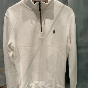 Vit långärmad tröja från Polo Ralph Lauren - Säljer en stilren vit långärmad tröja från Polo Ralph Lauren med dragkedja vid halsen. Tröjan har en broderad logotyp på bröstet och är perfekt för en avslappnad look. Passar bra till både jeans och chinos.