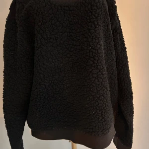 Svart fleecetröja från Monki - Cool svart fleece tröja från Monki i storlek L. Perfekt för kyliga dagar med sin mjuka och fluffiga textur. Tröjan har långa ärmar och en avslappnad passform. Använd men har mer att ge. Ett trevligt inslag i garderoben!