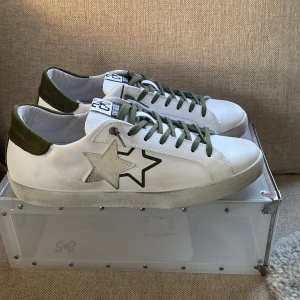Oanvända vita 2star skor - Säljer mina helt oanvända skor. Jag lägger ut dessa 15 minuter efter jag fått hem min beställning då dem var förstora och jag inte kunna skicka tillbaks dem. Der är ett par sygga vita sneakers från det italienska märket 2star med gröna snören och häl. Skorna har en stjärndetalj på sidan och en bekväm passform. Perfekta för en stilren look. Det kommer även med en snygg box och extra vita snören. Tveka inte att fråga vid minsta lilla fundering.🇮🇹🫡💥 