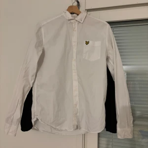 Vit skjorta från Lyle & Scott - Säljer en stilren vit skjorta från Lyle & Scott med en broderad logga på bröstfickan. Skjortan har långa ärmar och knappar framtill. Perfekt för en klassisk look.