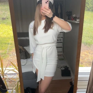 Vit klänning med knytband - Säljer denna vita klänning med knytband i midjan och trekvartsärmar. Går att ha till studenten eller finare tillfällen. Inte använd. Lappar kvar. 