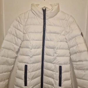Vit dunjacka från Tommy Hilfiger - Säljer en snygg vit dunjacka från Tommy Hilfiger. Perfekt för kyliga dagar! Jackan har fått lite sminkmärken i nacken se bild 3 och 5. Därav säljes den billigt då den var dyr i inköp. Garderobsrensning så kika gärna på övriga auktioner.
