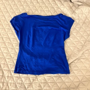 Blå topp med öppen rygg - Säljer en snygg blå topp med korta ärmar och en stilren öppen rygg. Perfekt för varma dagar eller en kväll ute. Toppen har en enkel och elegant design som gör den lätt att matcha med olika outfits.