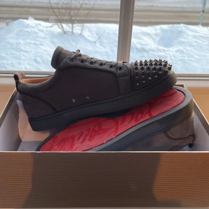 Svarta sneakers med nitar - Snygga svarta sneakers från Christian Louboutin med nitar på tån och den ikoniska röda sulan. Skorna har snörning och är tillverkade i ett elegant material som ger en lyxig känsla.