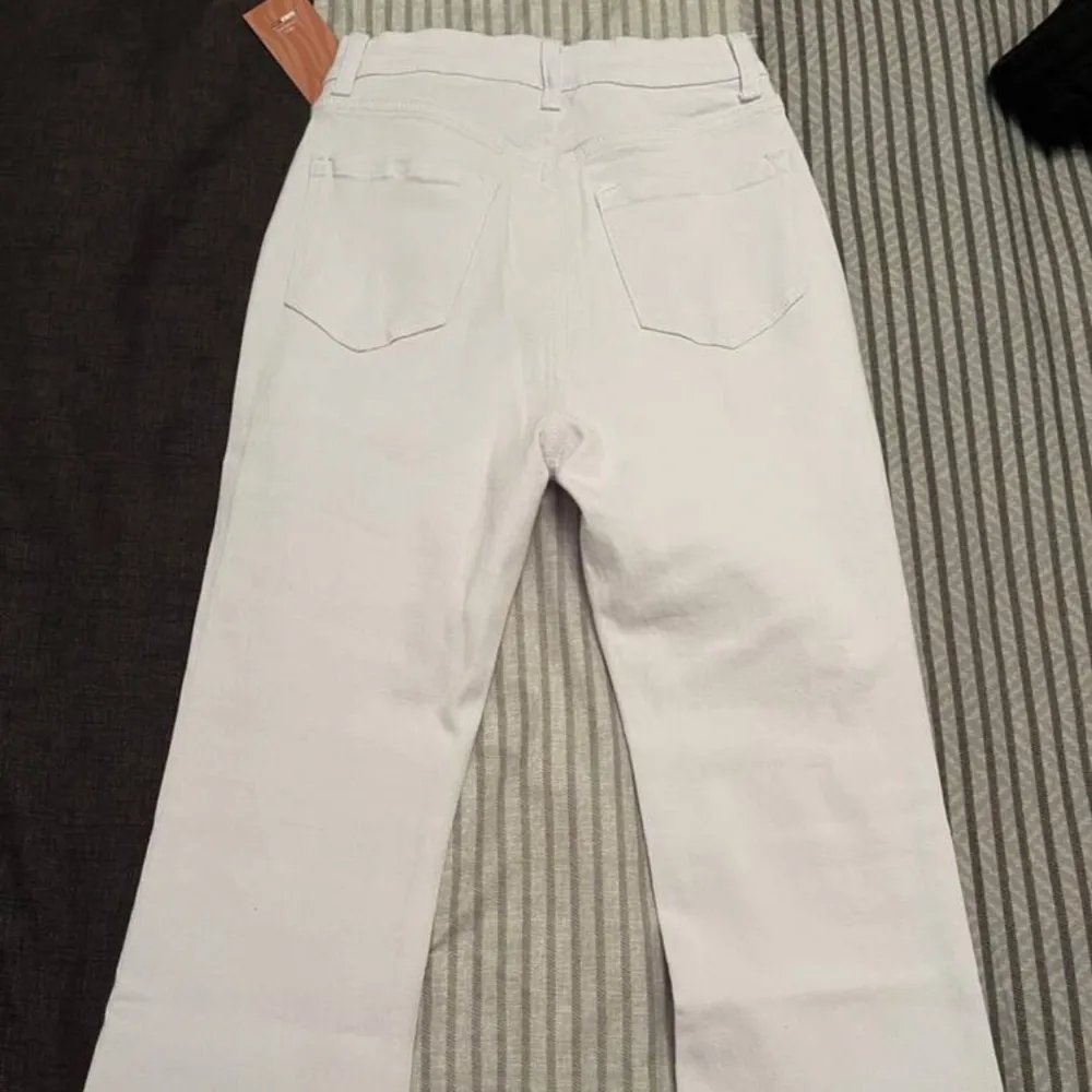 Snygga vita jeansbyxor med hög midja och bootcut-stil. Byxorna har en dragkedja framtill och klassiska bakfickor. Perfekta för en stilren look.. Farkut & Housut.