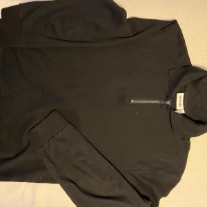 Svart tröja med dragkedja från Weekday - Säljer en stilren svart tröja från Weekday med dragkedja vid halsen. Tröjan har långa ärmar och en hög krage, perfekt för en minimalistisk look. Passar bra till både jeans och chinos.