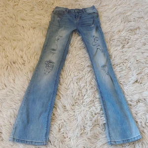 Ljusblå lågmidjade bootcut jeans med slitningar  - Midjemått rakt över: Ungefär 34 cm + stretch💞 Innerbenslängd: Ungefär 75-76 cm men går att sprätta upp för att lägga till lite längd💞 Grenhöjd: Ungefär 17 cm💞Världens snyggaste stretchiga ljusblå jeans med slitningar i modellen ”lowrise bootcut” som kan ses på näst sista sidan (litet rött märke där även men är på insidan och syns knappt)💞 Säljer då de är för små för mig😭😭 (ALLA BILDER ÄR MINA!)
