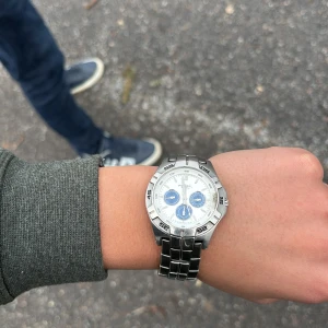 Silverfärgad klocka från Fossil - Snygg silverfärgad klocka från Fossil med metallarmband och vit urtavla. Klockan har tre blå subdialer och tydliga markeringar på boetten. Perfekt för den som gillar en stilren och modern look.