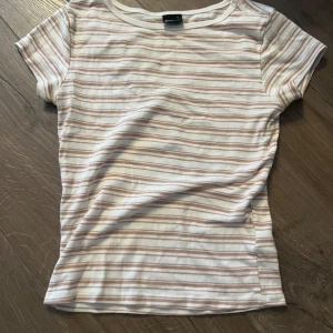 Randig t-shirt från Gina Tricot - Säljer en snygg randig t-shirt från Gina Tricot i storlek S. T-shirten har korta ärmar och ett klassiskt randigt mönster i beige och vit. Perfekt för en avslappnad stil.
