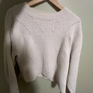 Beige stickad tröja från H&M - Säljer en snygg beige stickad tröja från H&M. Tröjan har en croppad design med ett unikt stickmönster och långa ärmar. Perfekt för kyligare dagar!