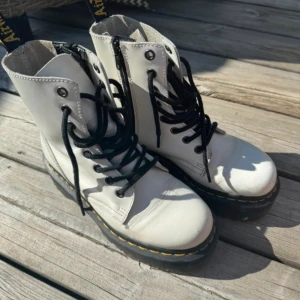 Vita boots med snörning och dragkedja Dr.Martens - Snygga vita boots från Dr. Martens med klassisk snörning och praktisk dragkedja på sidan. De har en robust sula med gul söm och är perfekta för en edgy stil.