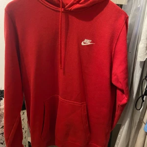 Röd hoodie från Nike - Säljer en snygg röd hoodie från Nike med klassisk logga på bröstet. Den har en känguruficka och justerbar huva med dragsko. Perfekt för en avslappnad stil.