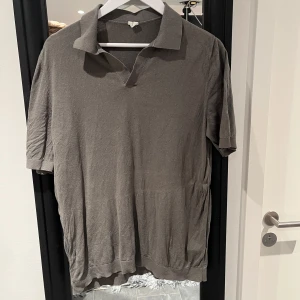 Grön pikétröja - Säljer en stilren gröngrå pikétröja med korta ärmar. Perfekt för en avslappnad och snygg look. Tröjan har en klassisk krage och är tillverkad i ett mjukt material. Från arket