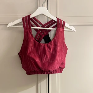 Mörk rosa sporttopp från XPDBLS - Snygg mörk rosa sporttopp från XPDBL med prickigt mönster och korsade axelband. Toppen har en elastisk nederkant för extra stöd och är perfekt för träning. Ser mer röd ut på bilden än vad den är. Lappen har klippts av men det är storlek M