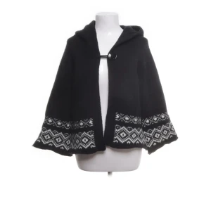 Svart poncho med mönster - Snygg svart poncho med vitt geometriskt mönster längs nederkanten. Ponchon har en enkel knäppning framtill och är perfekt för kyliga dagar. Den är både stilren och bekväm att bära.