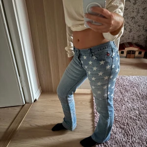 Vintage ljusblå Miss Sixty jeans med stjärnmönster - Snygga ljusblå jeans med ett coolt stjärnmönster på benen. De har en lågmidjad passform och en bootcut-stil. Perfekta för att sticka ut med en unik look.