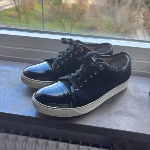 Svarta sneakers från Lanvin - Snygga svarta sneakers från Lanvin med glansig tå. Storleken är 7 och skicket är 7/10. Skorna har fått en lagning på insidan av hålan och funkar klockrent. Nypris 5.000kr
