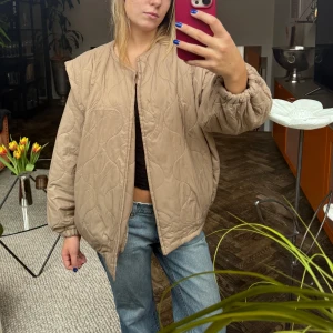 Beige quiltad jacka - Säljer en beige quiltad jacka med en oversized passform. Jackan har långa ärmar och en stilren design utan synliga knappar eller dragkedja. Perfekt för en avslappnad look.
