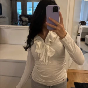 Vit långärmad topp från Ralph Lauren - Säljer en elegant vit långärmad topp från Ralph Lauren med volangdetaljer framtill. Toppen har en normal passform och är tillverkad i ett mjukt material. Dets tår storlek (12-14)