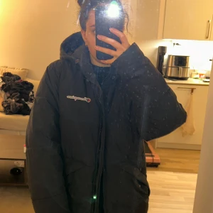Svart dunjacka från Champion - Säljer en svart dunjacka från Champion. Jackan har en pufferdesign med dragkedja och en stor huva för extra värme. Perfekt för kalla dagar.