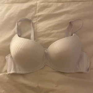 Vit randig bh med rosett - Säljer en vit pushup bh med diskreta ränder och en söt rosett mellan kuporna. Den har justerbara axelband för bästa passform. 