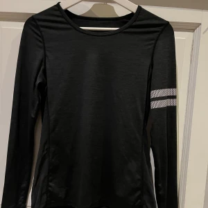 Svart långärmad tröja från Stronger - Säljer en svart långärmad tröja från Stronger med en stilren design. Den har en vit randdetalj på ärmen. Perfekt för träning eller en aktiv vardag. Tröjan är tillverkad i ett syntetmaterial som andas och ger en skön passform. Från rök/djurfritt hem!