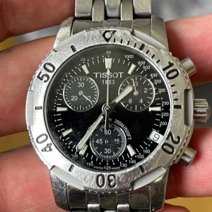 Tissot klocka i rostfritt stål - Säljer en robust Tissot klocka med svart urtavla och kronograf. Boetten och armbandet är i rostfritt stål. Klockan är vattentät upp till 200m och har safirglas. Perfekt för den som söker en stilren och funktionell klocka.