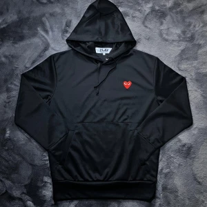 CDG Hoodie - Säljer en svart hoodie från Comme des Garçons i nyskick med det ikoniska röda hjärtat på bröstet. Perfekt för en avslappnad look. Storlek L men sitter mer som M. Nypris 3100kr. Skick 10/10. Pris går att diskutera✅