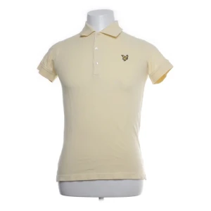 Beige pikétröja från Lyle & Scott - Säljer en stilren beige pikétröja från Lyle & Scott. Tröjan har en klassisk krage och korta ärmar med en liten logotyp på bröstet. Tillverkad i 100% bomull för en bekväm passform. Perfekt för en avslappnad look.