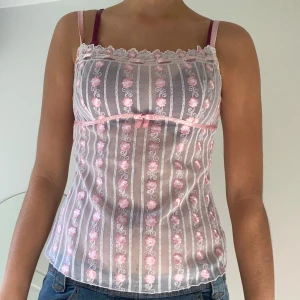 Söt blommig linne i rosa och vitt - Säljer en superfin linne i rosa och vitt med blommigt mönster. Den har smala axelband och en söt liten rosett framtill. Perfekt för sommardagar eller som ett sött lager under en kofta. Så söt!!!