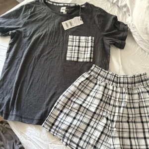 Rutig pyjamasshorts från Next - Säljer ett par superbekväma och stilrena pyjamasshorts från Next. De är vita med ett klassiskt svart rutmönster och har en elastisk midja för extra komfort. Perfekta för en mysig hemmakväll eller sommarens varma nätter!