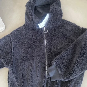 Svart teddyjacka från Topshop - Mysig svart teddyjacka från Topshop i storlek S. Perfekt för kyliga dagar med sin fluffiga och varma design. Jackan har en dragkedja framtill och en bekväm huva. Den är i nyskick och redo att hålla dig varm hela vintern!
