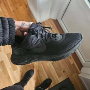 Svarta Nike sneakers - Säljer ett par svarta Nike sneakers i nyskick, endast använda en gång.. De har en stilren design med snörning och är perfekta för både vardag och träning. Skorna är bekväma och har en slitstark sula.