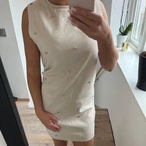 Beige ärmlös klänning med pärlor - Säljer en superfin beige klänning med pärldetaljer. Den är ärmlös och har en tight passform som framhäver figuren. Perfekt för festliga tillfällen! Klänningen är i nyskick, skriv för fler bilder eller frågor❤️