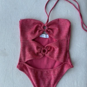 Rosa body från Bershka - Superfin rosa body från Bershka i storlek S. Den har en unik design med två knutna detaljer framtill som ger en snygg och trendig look. Materialet känns mjukt och bekvämt mot huden. Ett måste för din badgarderob! 💖