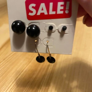 Svarta örhängen i set - Säljer ett set med svarta örhängen. Setet innehåller ett par stora runda studs och ett par hängande örhängen med små svarta plattor. Perfekt för både vardag och fest! Passa på att fynda på rea!