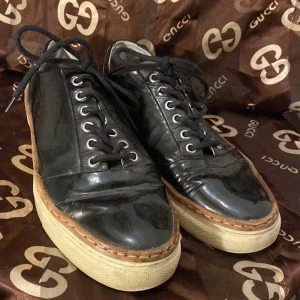 Svarta sneakers från Whyred - Säljer ett par svarta sneakers från Whyred i skinn. De har en snygg och stilren design med snörning och en vit sula som ger en cool kontrast. Perfekta för både vardag och fest! Skorna är i bra skick och redo för nya äventyr.