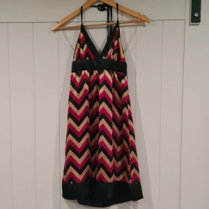Mönstrad klänning med zickzackmönster - Säljer en snygg klänning med zickzackmönster i svart, beige och vinröd. Den har en v-ringad hals och smala axelband. Klänningen är i ett lätt och silkigt material.