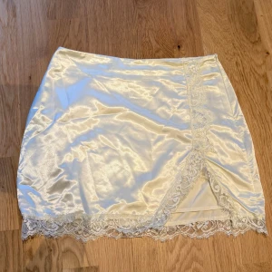 Satinkjol med spets - En kort satinkjol med slits och spetsdetaljer. Storlek medium och dradkedja på sidan.  Super bra skick och ber om ursäkt för de lite stressat tagna bilderna!!💗😄
